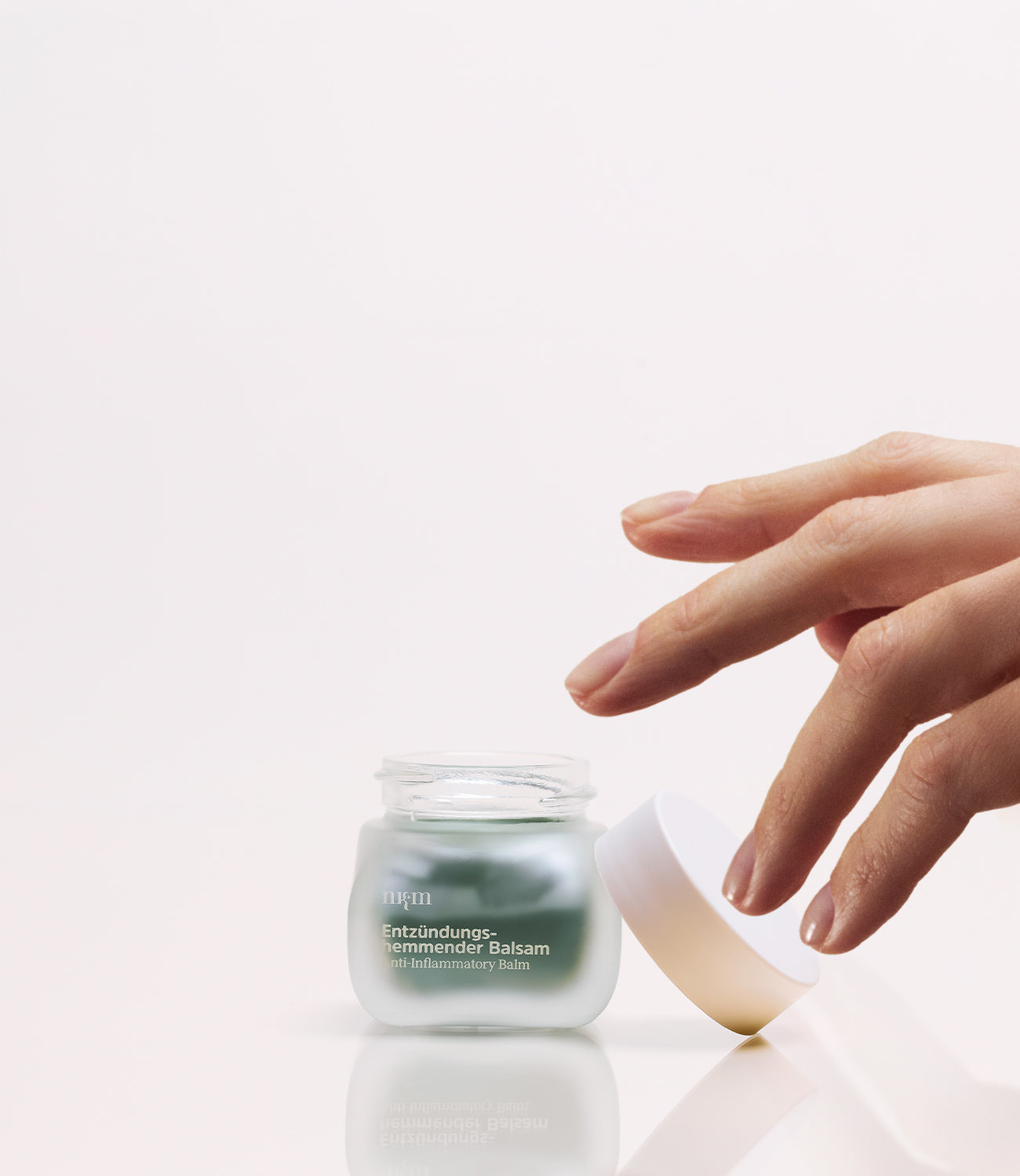 Entzündungshemmender Balsam und eine Hand, die nach dem Tiegel greift