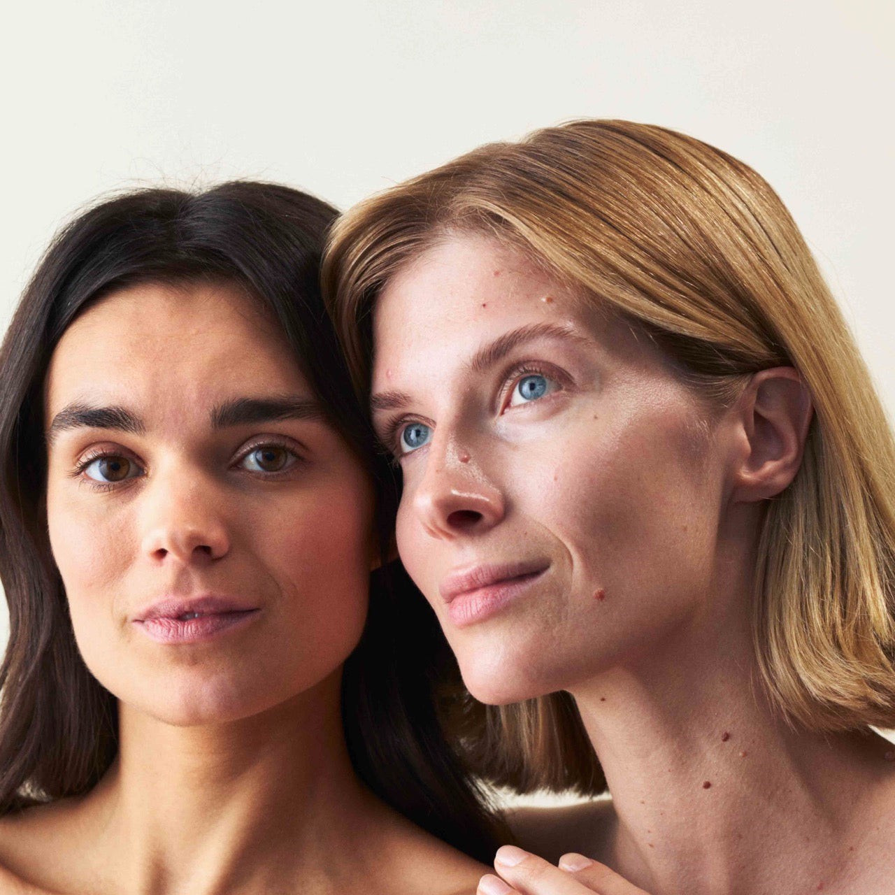 Zwei Frauen, die aneinander lehnen und in die Kamera schauen, die eine hat normale Haut und die andere hat Mischhaut.