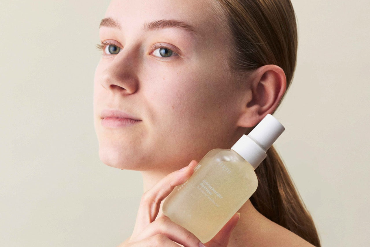 Eine Frau hält ein Gesichtsreiniger "Erfrischender Reiniger" in der Hand neben ihrem Gesicht