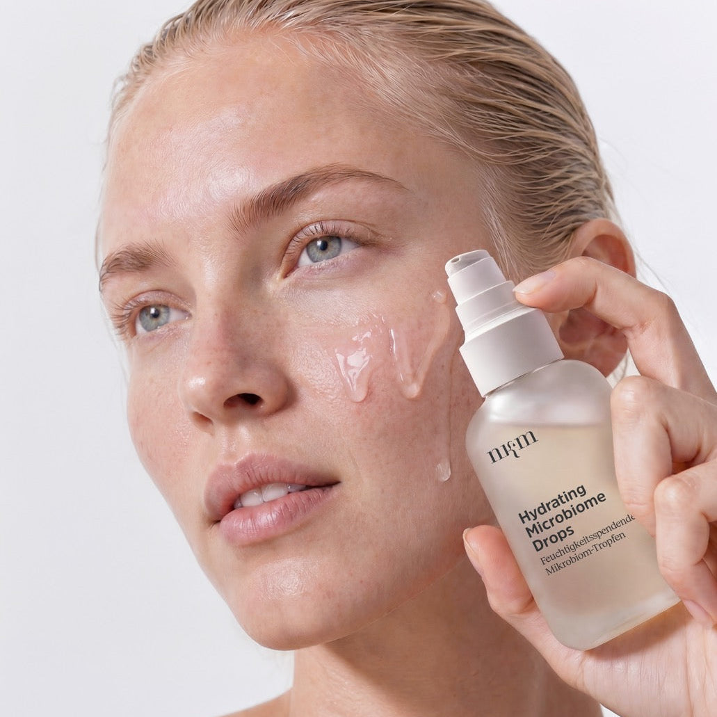 Frau mit blonden Haaren hält die Microbiome Drops von nkm in der Hand. Auf ihrer Wange sieht man die Konsistenz der Drops