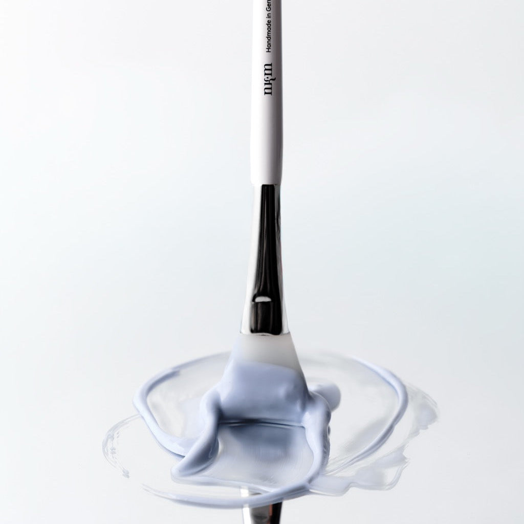 Pinsel mit nkm Logo verstreicht blaue Maske