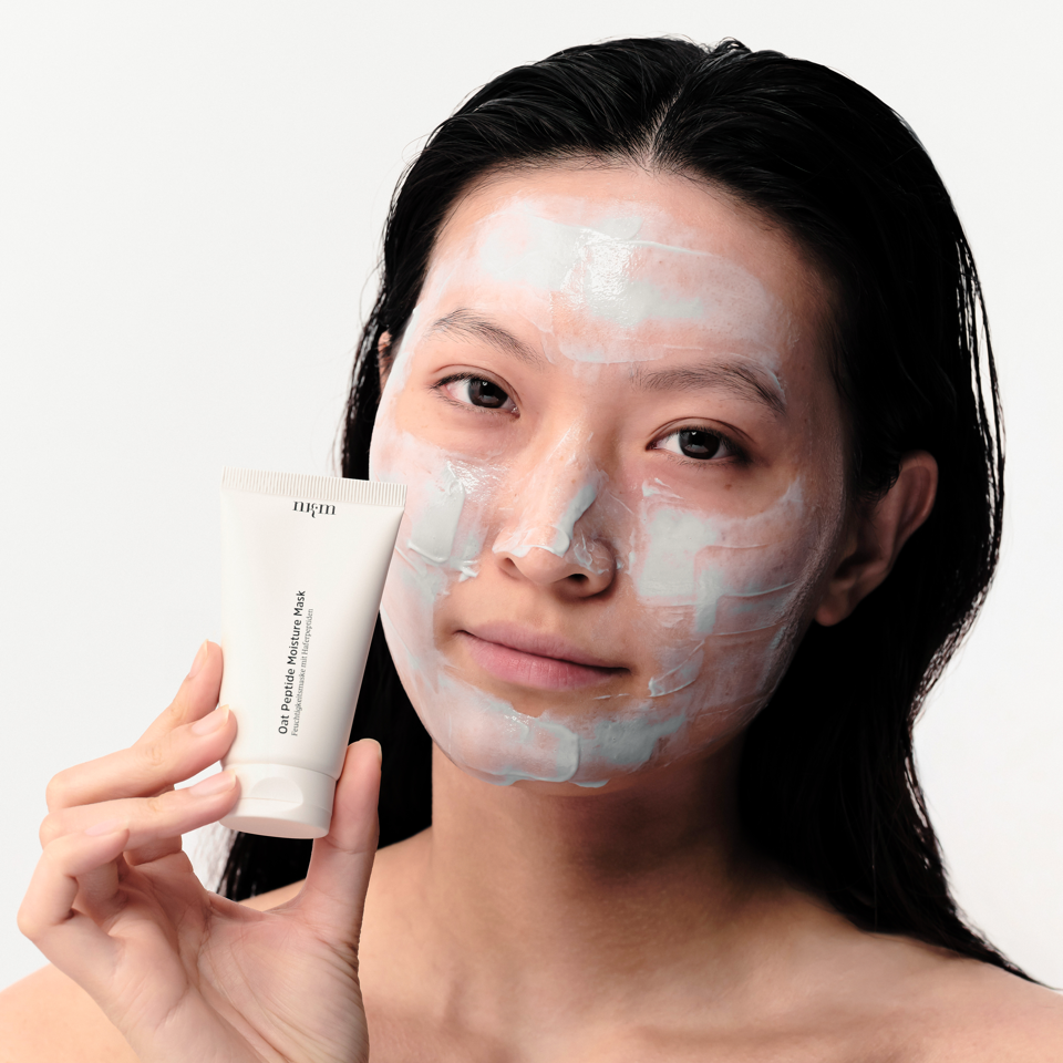Frau mit Oat Peptide Moisture Mask aufgetragen im Gesicht. Sie hält die Tube in der Hand