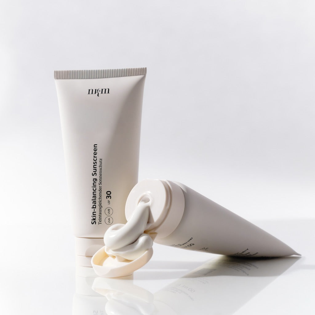 Skin-balancing Sunscreen von nkm. Einmal Tube stehend und einmal Tube liegend mit Konsistenz, die aus der Flasche dgedrückt wird