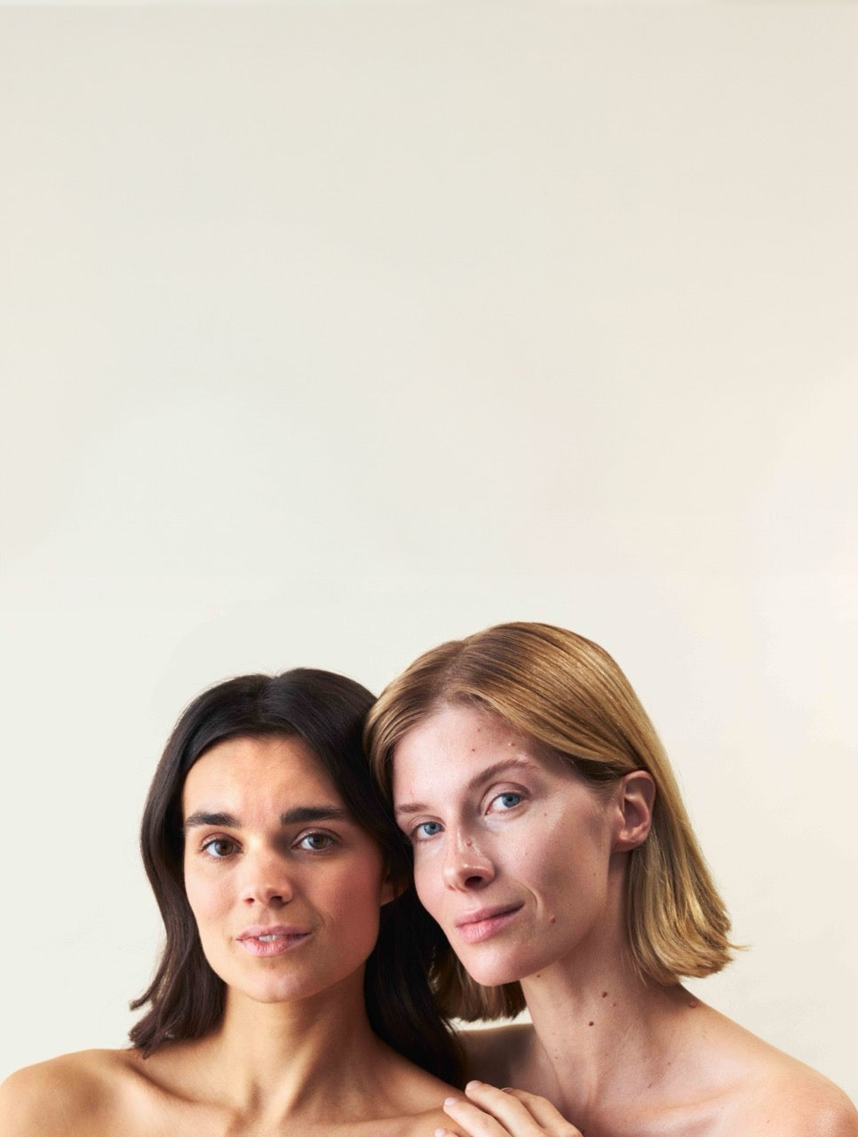 Zwei Frauen, die aneinander lehnen und in die Kamera schauen, die eine hat normale Haut und die andere hat Mischhaut.