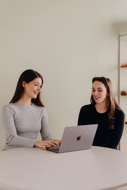 Zwei Frauen, die am Schreibtisch sitzen und miteinander reden.