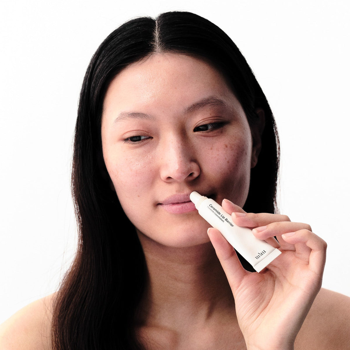 Frau mit dunklen Haaren trägt Ceramide Lip Barrier auf ihre Lippen auf