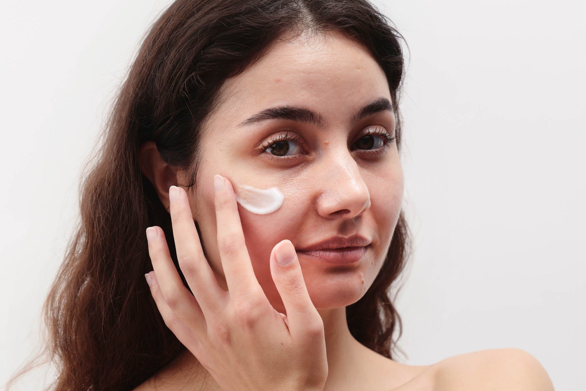 Frau mit dunkelbraunen Haaren trägt Creme im Gesicht auf