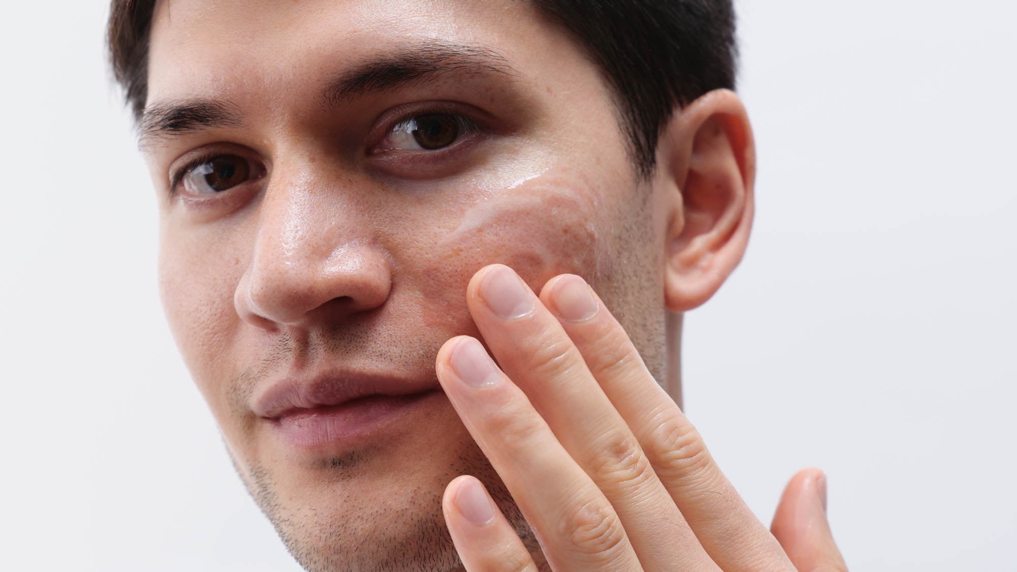 Mann mit dunklen Haaren trägt Gelcreme im Gesicht auf