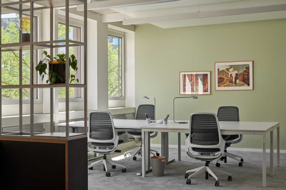 Office mit Schreibtischen und grüner Wand im Hintergrund