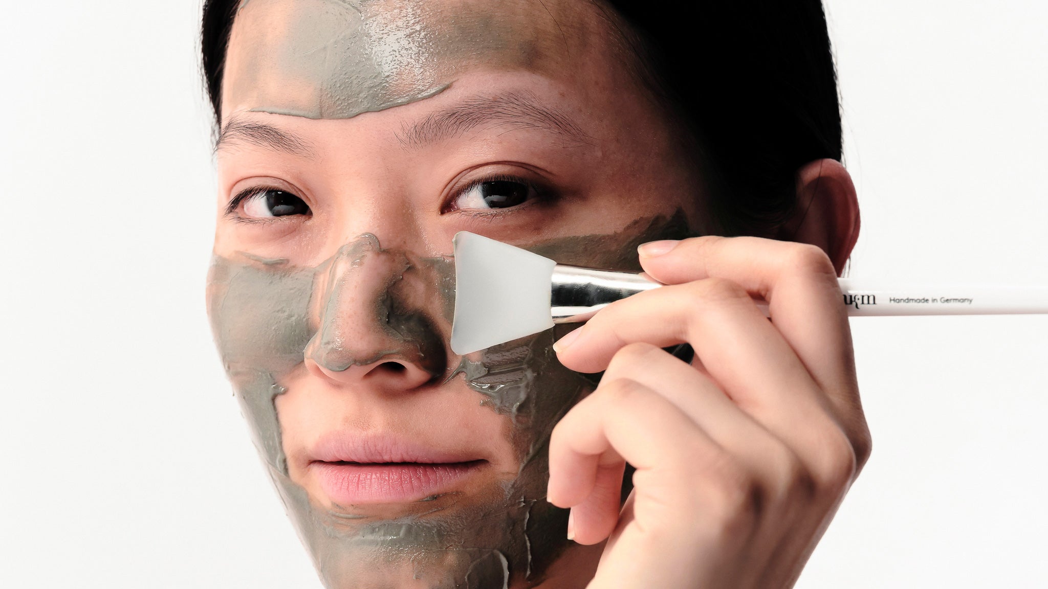 Frau hat Salicylic Pore Refining Mask aufgetragen und hält Pinsel mit nkm Logo ans Gesicht