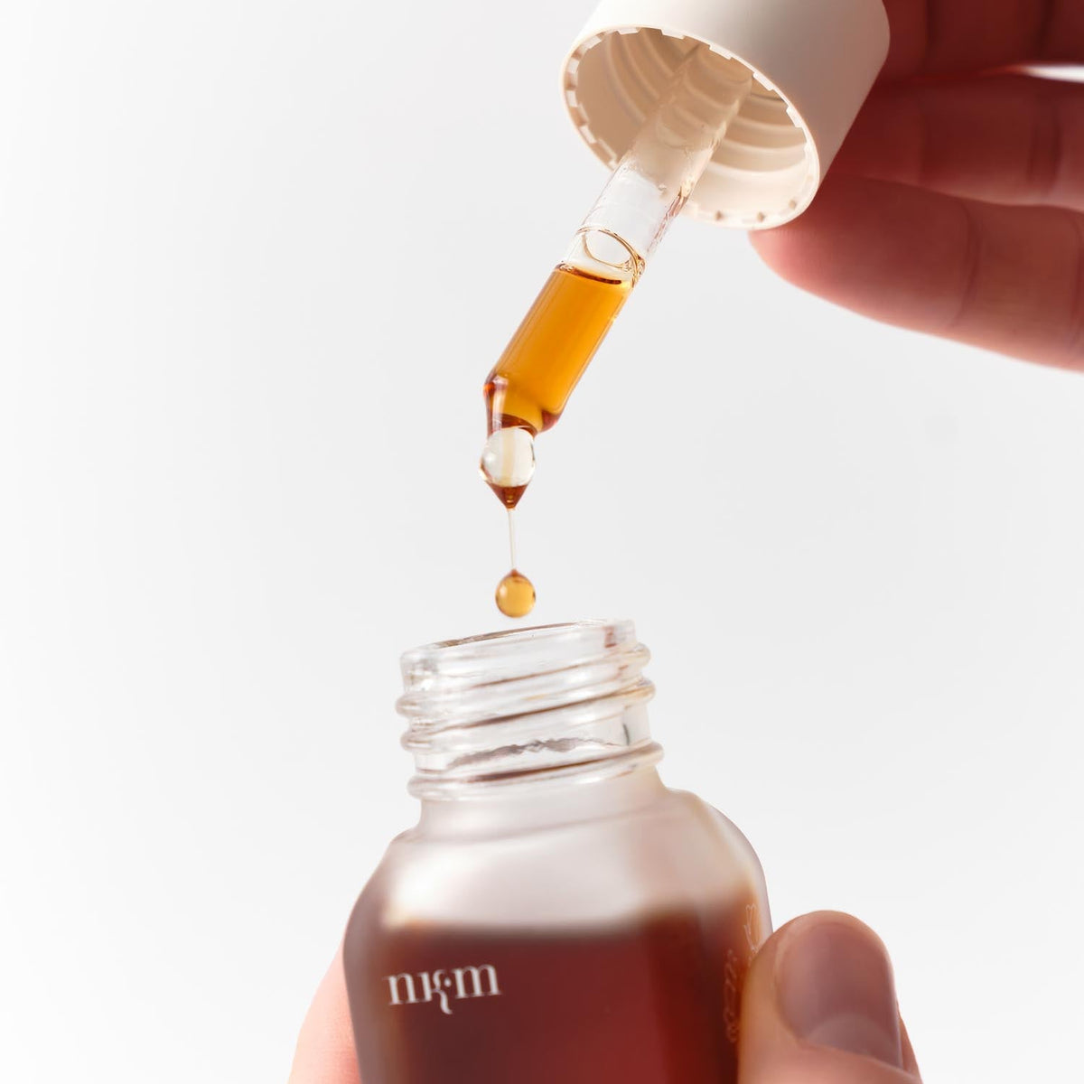 Eine Hand hält eine Pipette über eine geöffnete Flasche mit braunem Intensivöl Neu der nkm Naturkosmetik München GmbH und gibt einen Tropfen zur Vorbeugung vorzeitiger Faltenbildung ab.