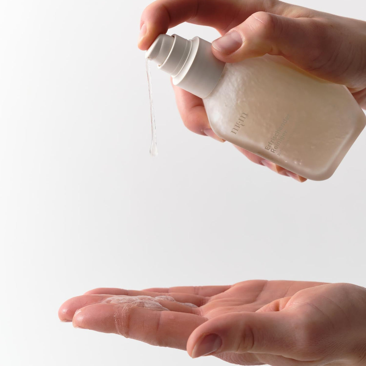 Eine Hand verteilt Erfrischender Reiniger Neu von nkm Naturkosmetik München GmbH auf einer anderen Handfläche vor weißem Hintergrund - ideal für reife Haut und trockene Haut.