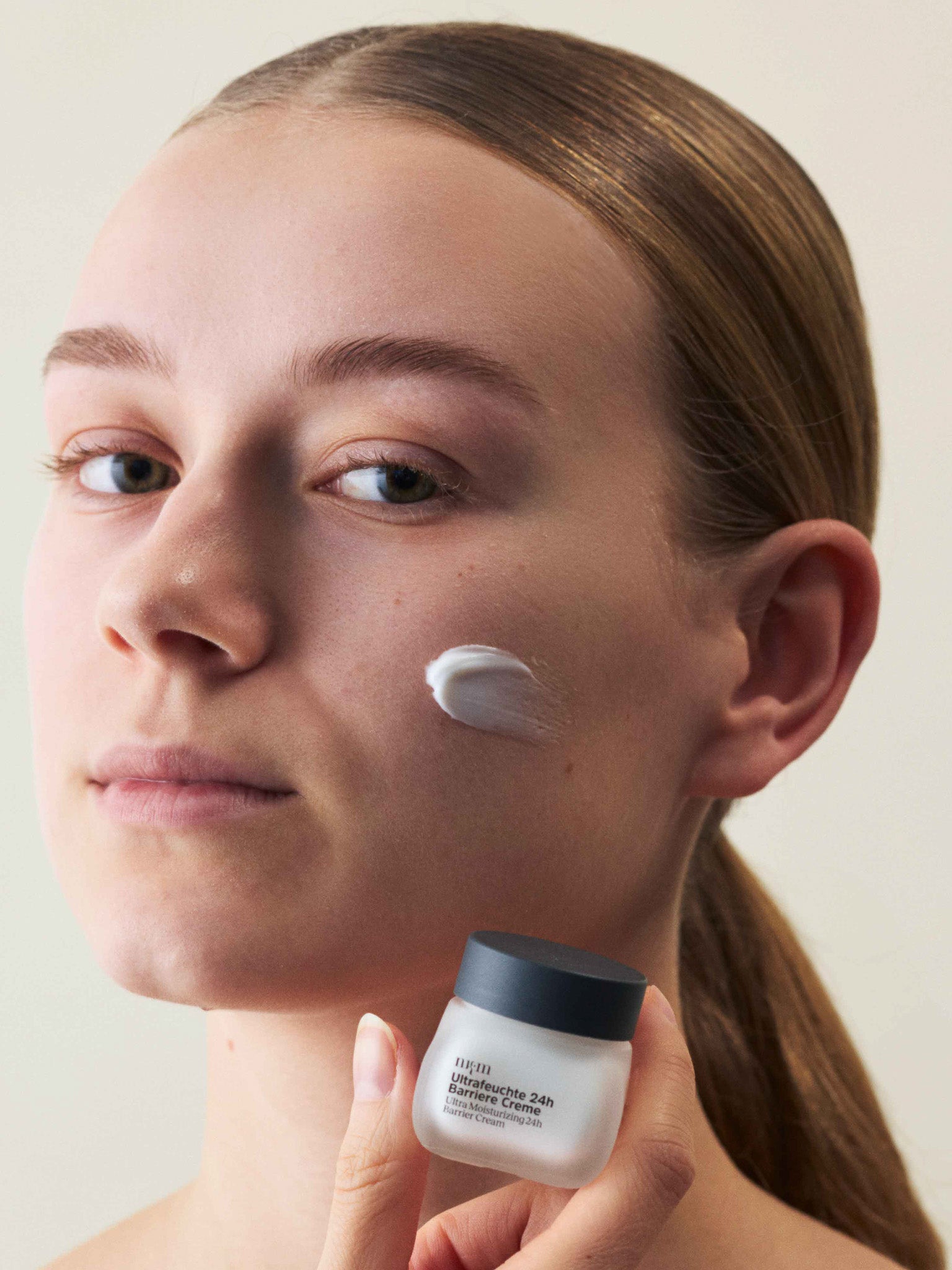 Eine Frau, die die Reisegröße Ultrafeuchte 24h Barriere Creme in der Hand hält