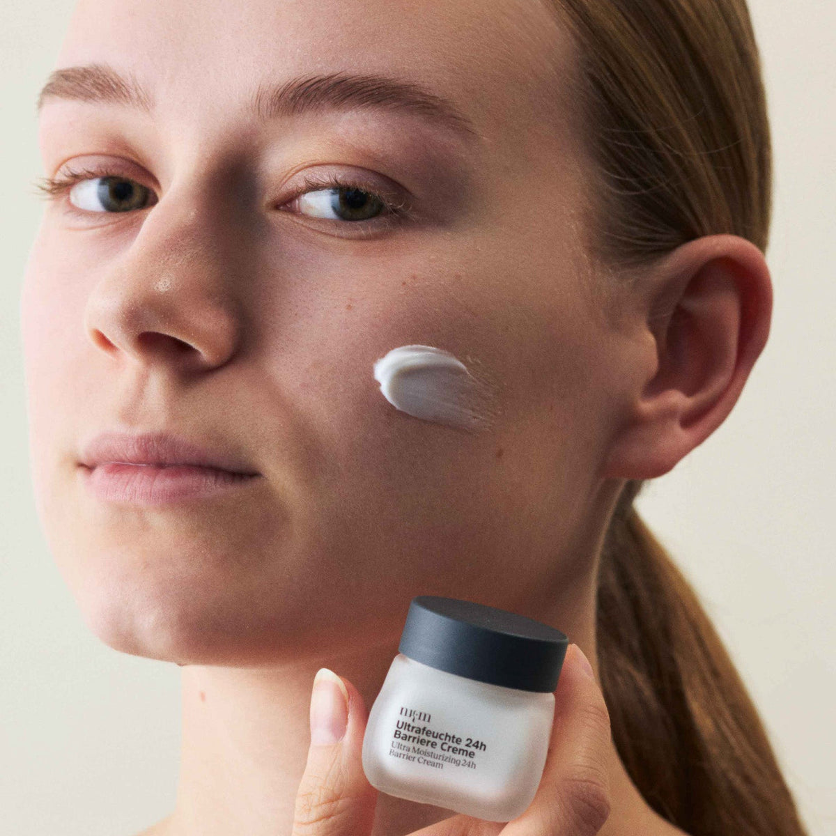 Eine Frau, die die Reisegröße Ultrafeuchte 24h Barriere Creme in der Hand hält
