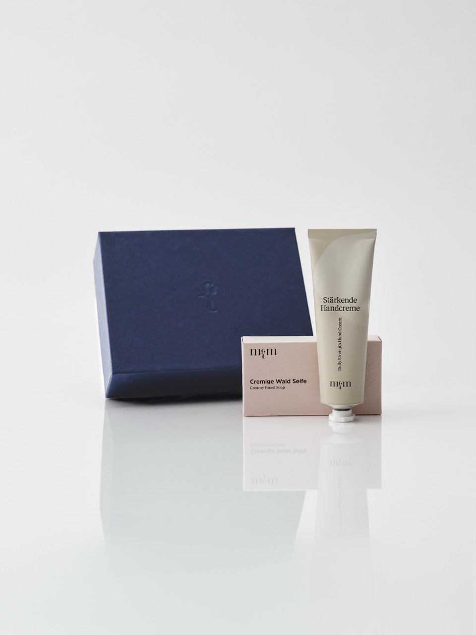 Eine dunkelblaue Box und davor die Cremige Wald Seife und die Stärkende Handcreme von nkm