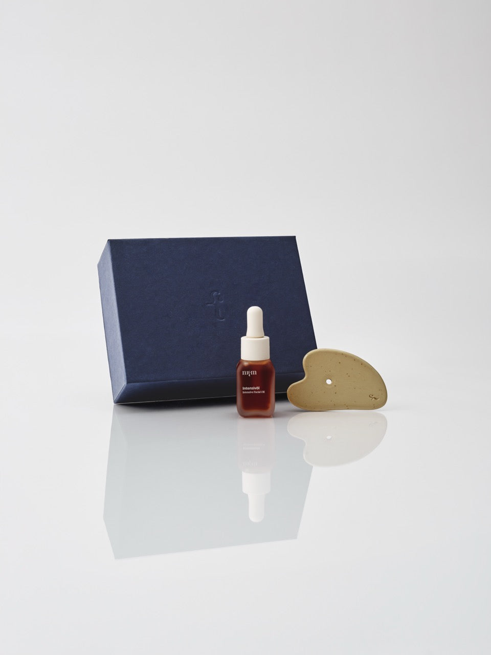Eine dunkelblaue Box und davor das Intensivöl und der Gua Sha von nkm