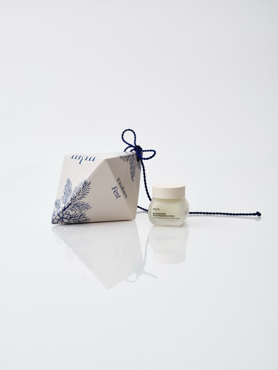 Weißes Weihnachtsornament mit aufgemalten blauen Tannenzweigen, daneben die Erneuernde Feuchtigkeitscreme