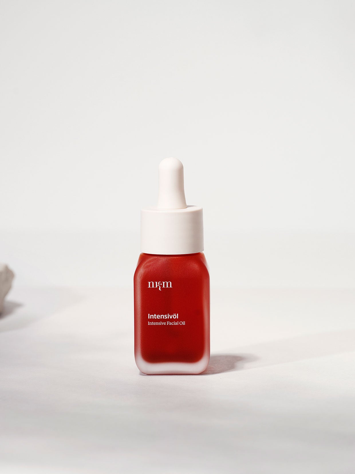 Eine rote Flasche nkm Naturkosmetik München GmbH Intensivöl mit pflegenden Hagebutten und Rosenöl, verschlossen mit einem weißen Tropfverschluss, vor hellem Hintergrund.