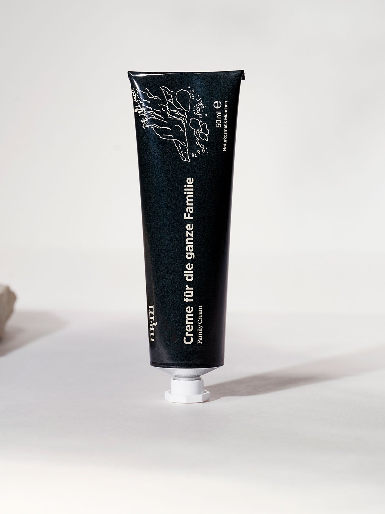 Auf einer hellen Fläche steht eine schwarze Tube "Creme für die ganze Familie" der nkm Naturkosmetik München GmbH mit minimalistischer weißer Schrift und Illustrationen - ideal für die Intensivpflege und sanft genug für zarte Babyhaut.