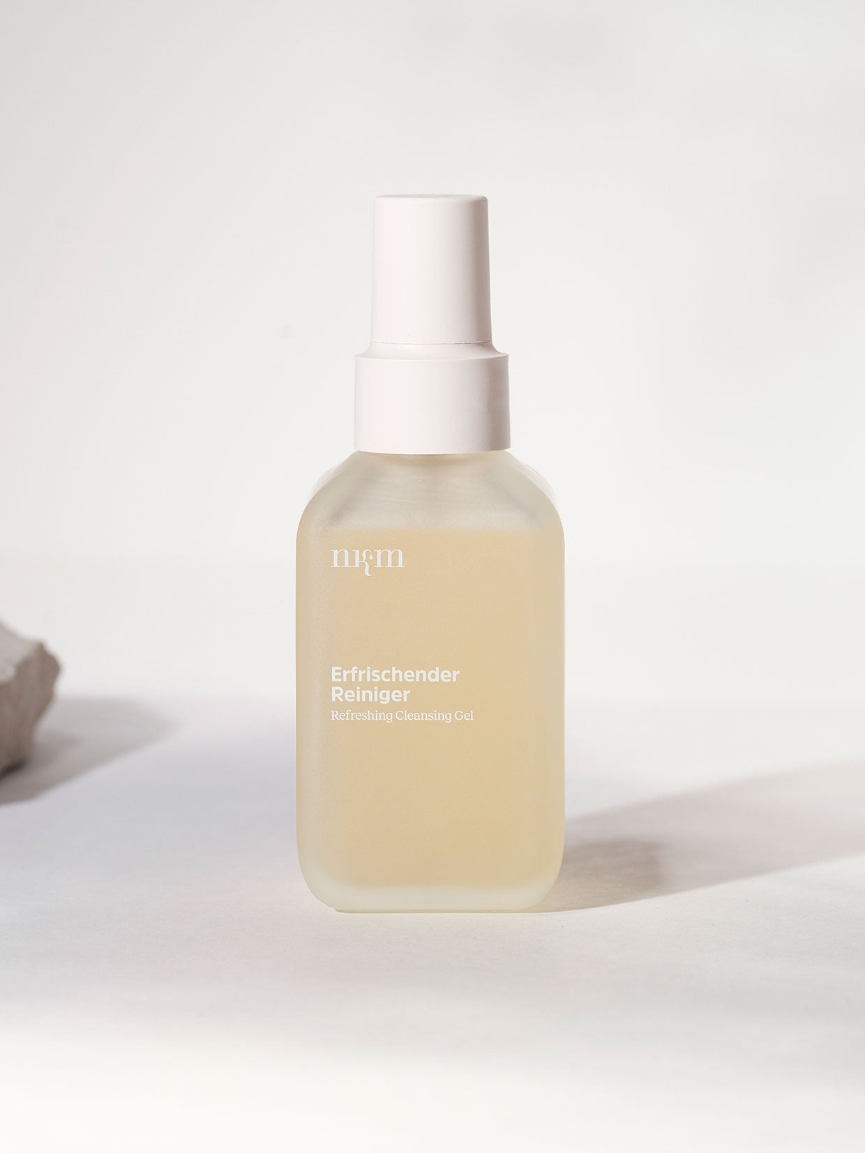 Eine gefrostete Flasche des Erfrischender Reiniger mit Zitronengras der nkm Naturkosmetik München GmbH steht auf einem hellen Hintergrund, perfekt für trockene Haut.