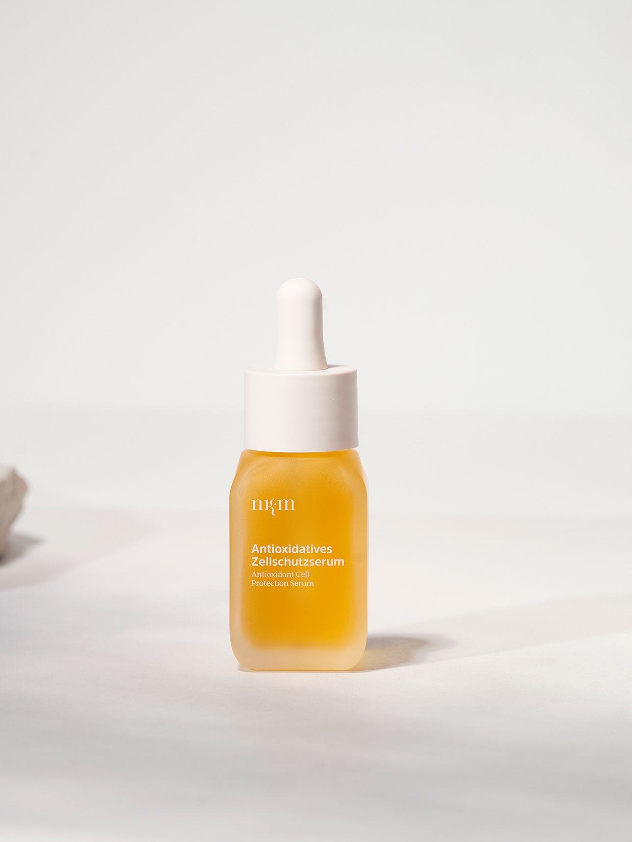 Eine gelbe Serumflasche der nkm Naturkosmetik München GmbH mit der Aufschrift Antioxidatives Zellschutzserum mit Resveratrol und Antioxidantien und weißem Tropfverschluss steht auf hellem Hintergrund.