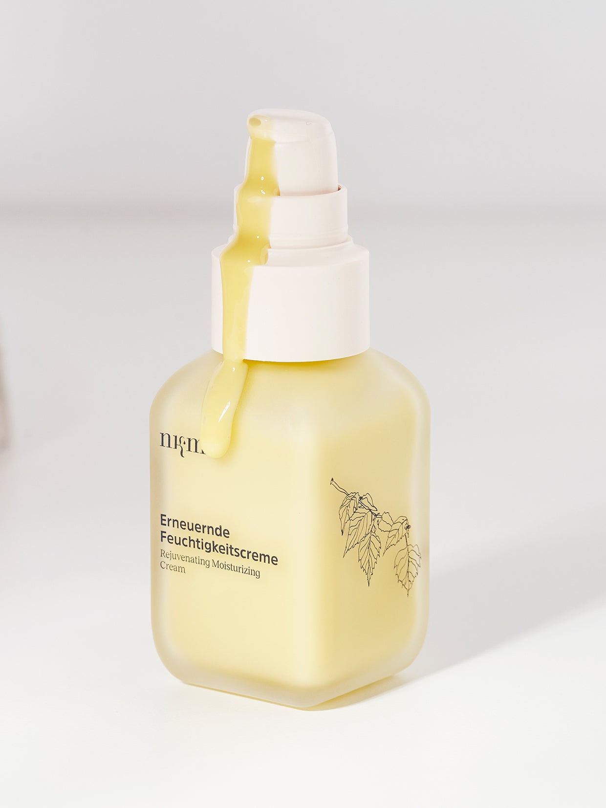 Ein gelber Flakon der nkm Naturkosmetik München GmbH Erneuernde Feuchtigkeitscreme mit aus der Pumpe fließender Creme, die die intensive Feuchtigkeitszufuhr für Ihre Hautpflege hervorhebt, vor einem weißen Hintergrund.