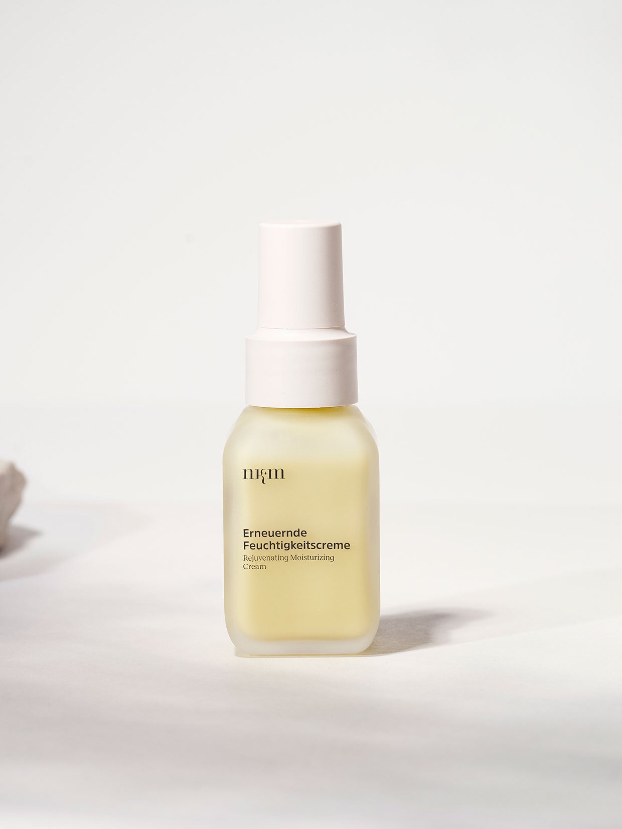 Ein gefrosteter Flakon der "Erneuernden Feuchtigkeitscreme" der nkm Naturkosmetik München GmbH mit Hyaluronsäure, weißer Pumpe und minimalistischem Etikett - ideal für eine effektive Hautpflege auf hellem Grund.