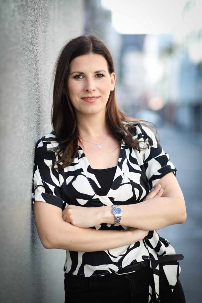Frau mit dunklen Haaren an Wand lehnend
