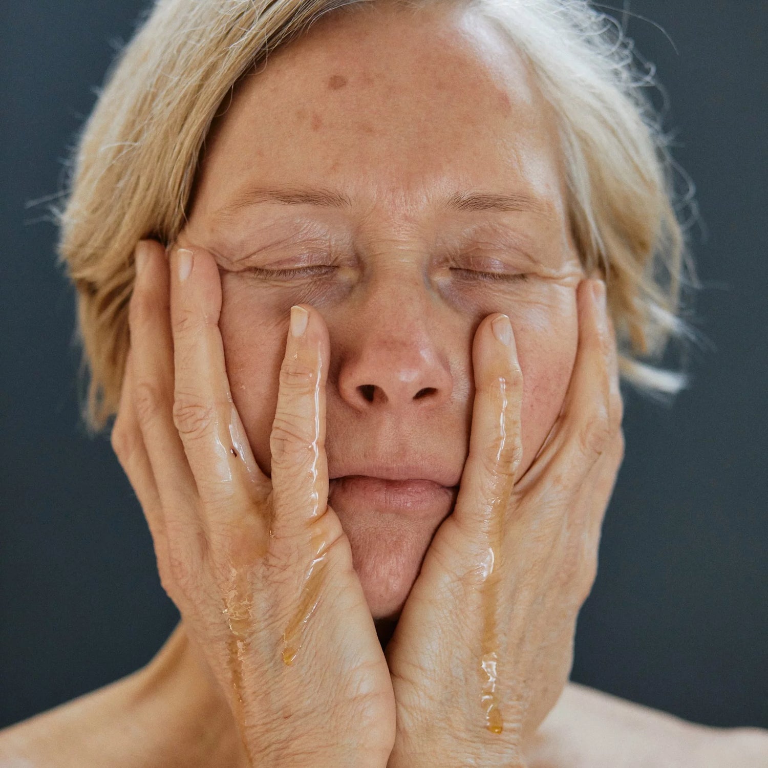 Frau mit reifer Haut hält Hände mit Öl aufs Gesicht