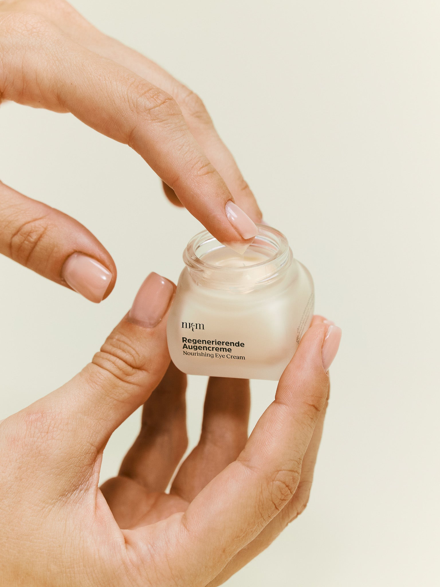 Hand hält Regenerierende Augencreme und nimmt Produkt mit Finger auf