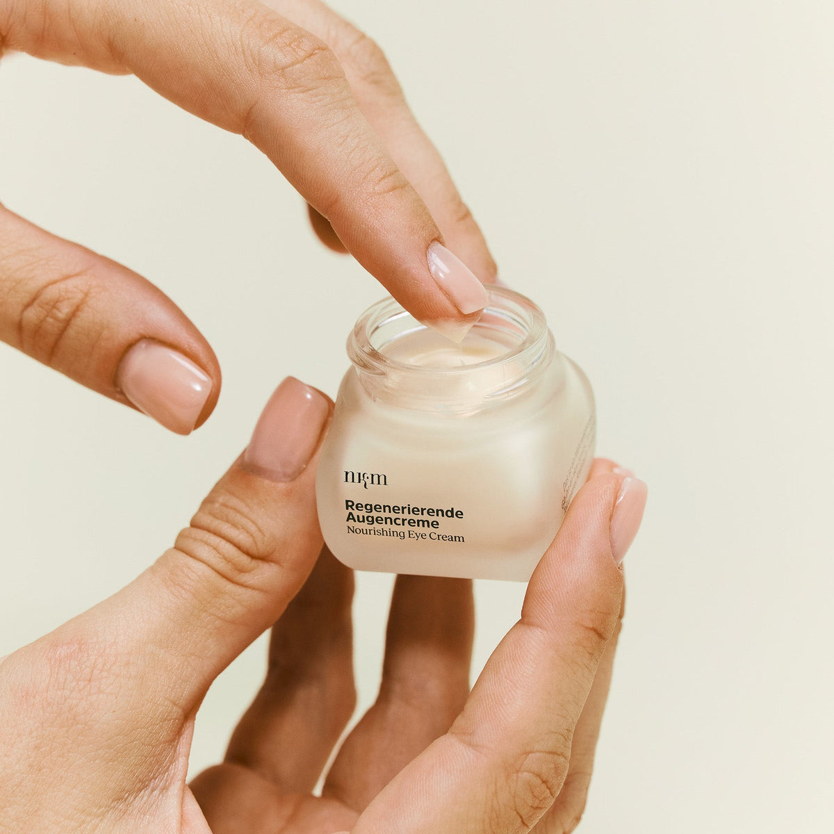 Hand hält Regenerierende Augencreme und nimmt Produkt mit Finger auf