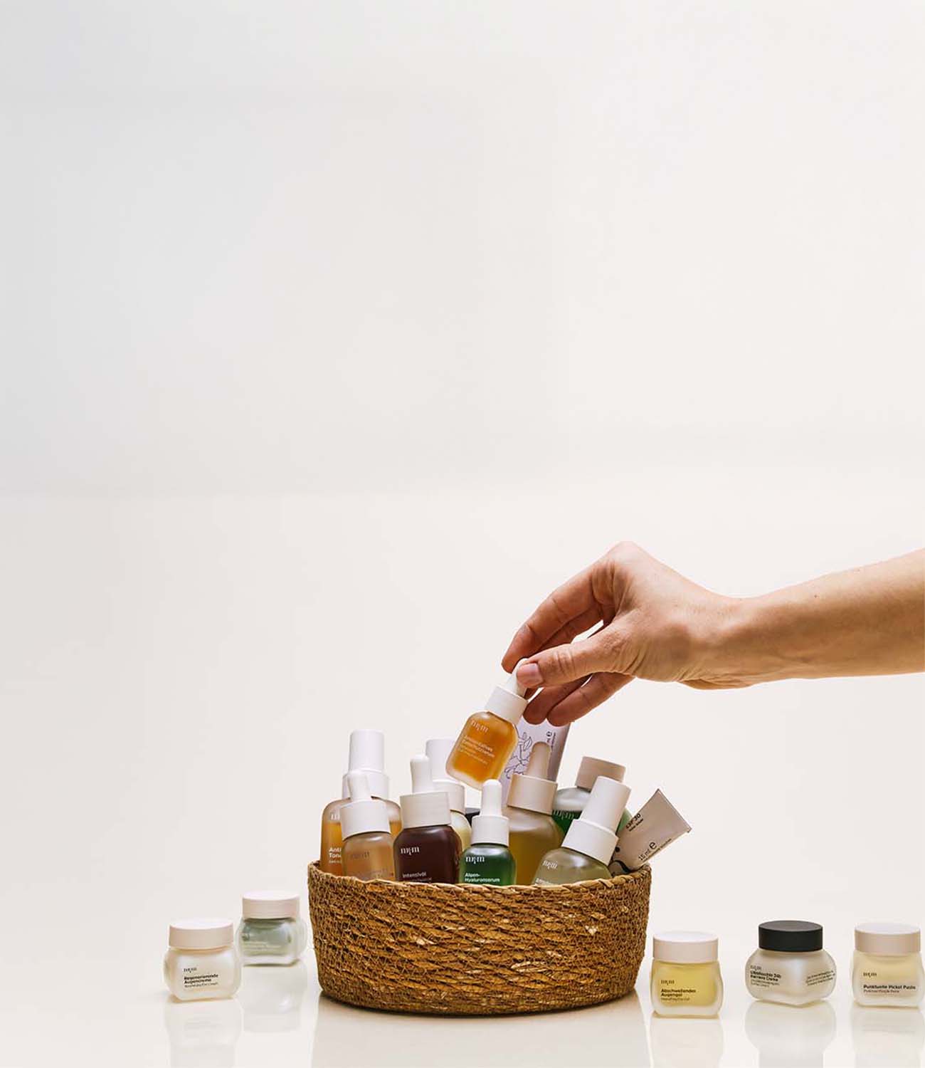 Eine Hand greift sich ein Serum aus einem geflochtenen Korb mit nkm Produkten