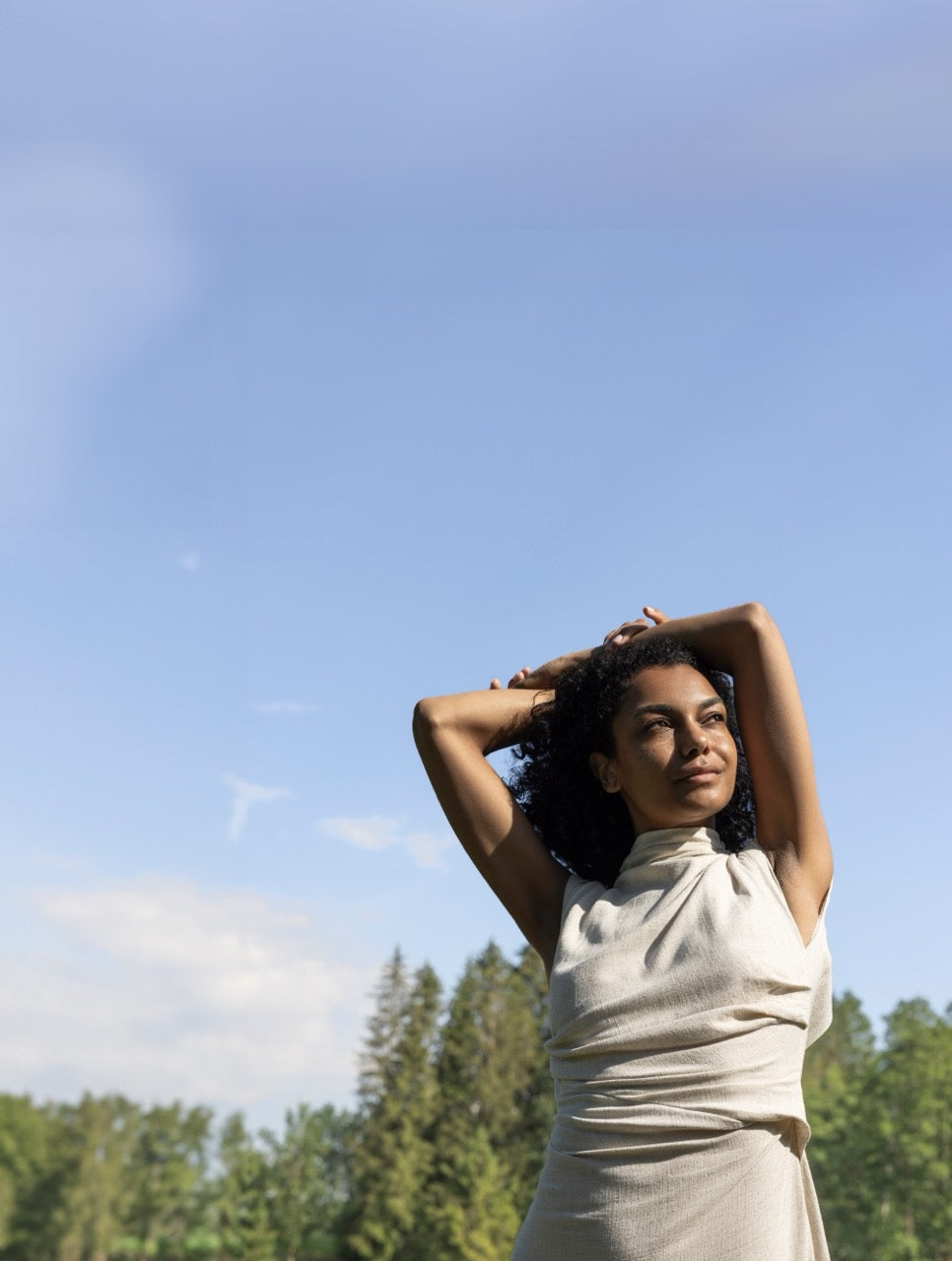 Eine Frau steht vor blauem Himmel und Bäumen