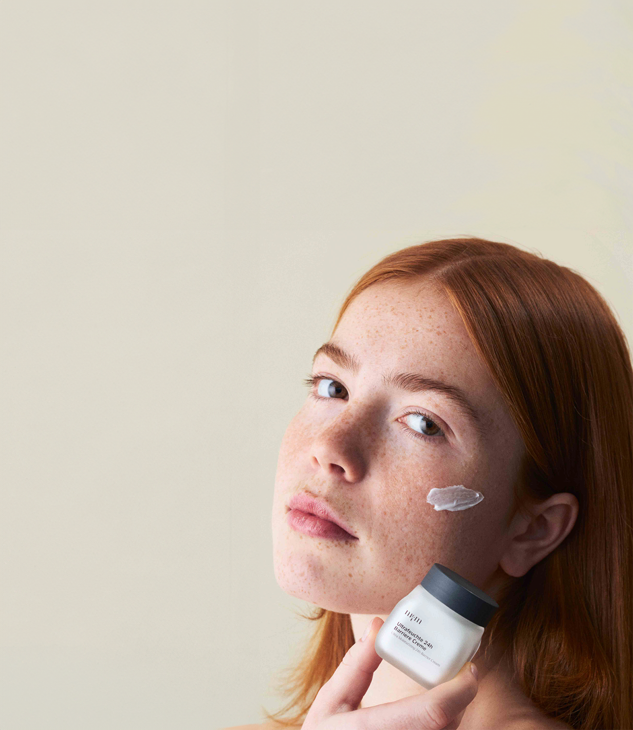 Eine Frau, die die Ultrafeuchte 24h Barriere Creme auf dem Gesicht trägt und die Flasche in der Hand