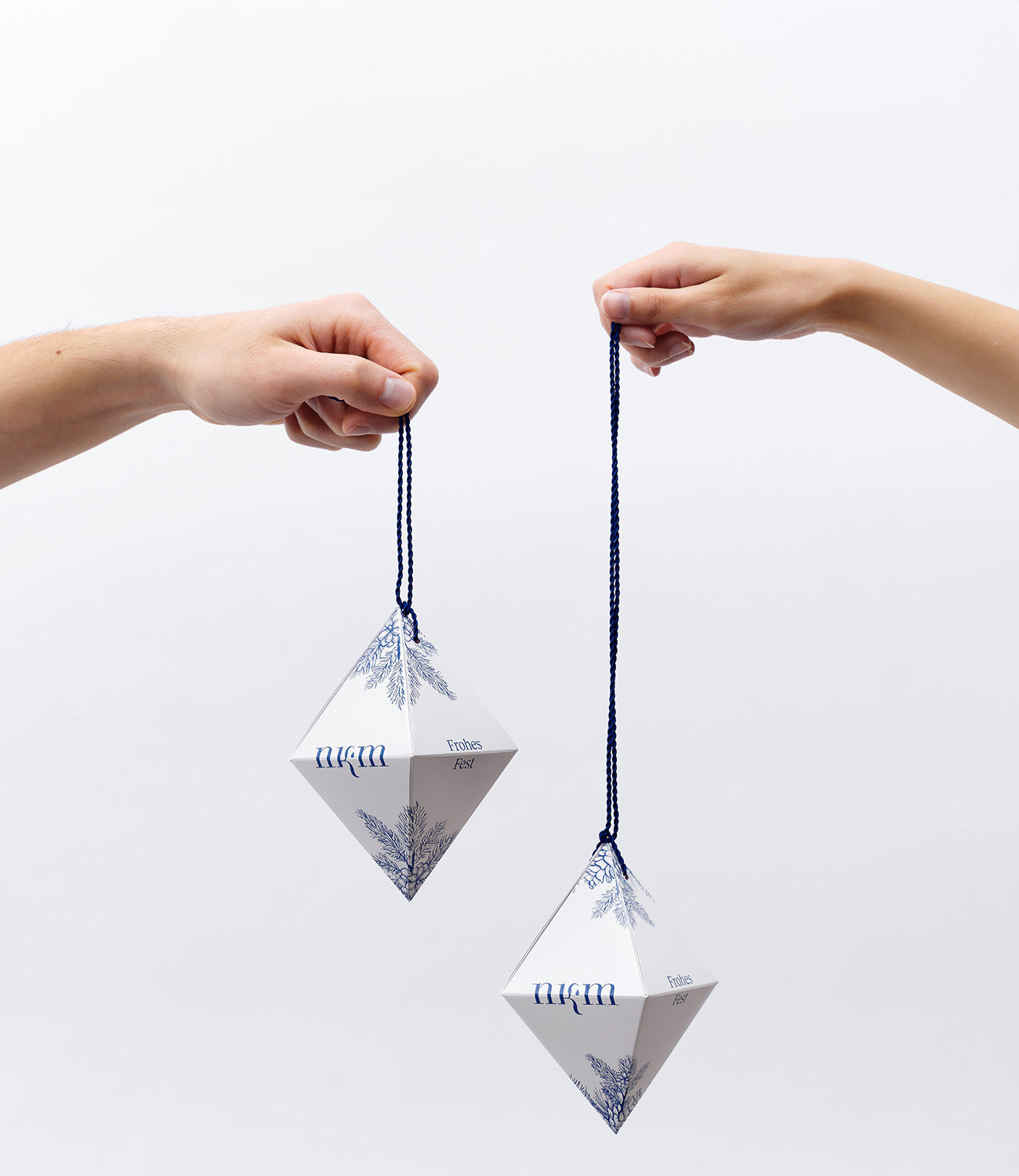 Zwei Hände Halten je ein weihnachtliches Ornament mit blauen, aufgemalten Zweigen