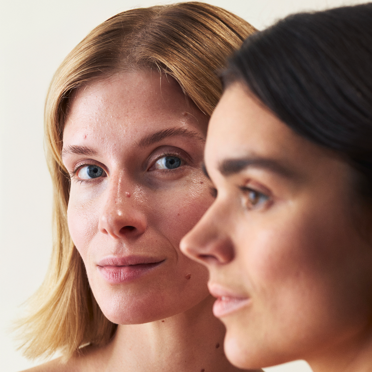 Zwei Frauen, die hintereinander stehen, die eine schaut nach links und die andere direkt in die Kamera