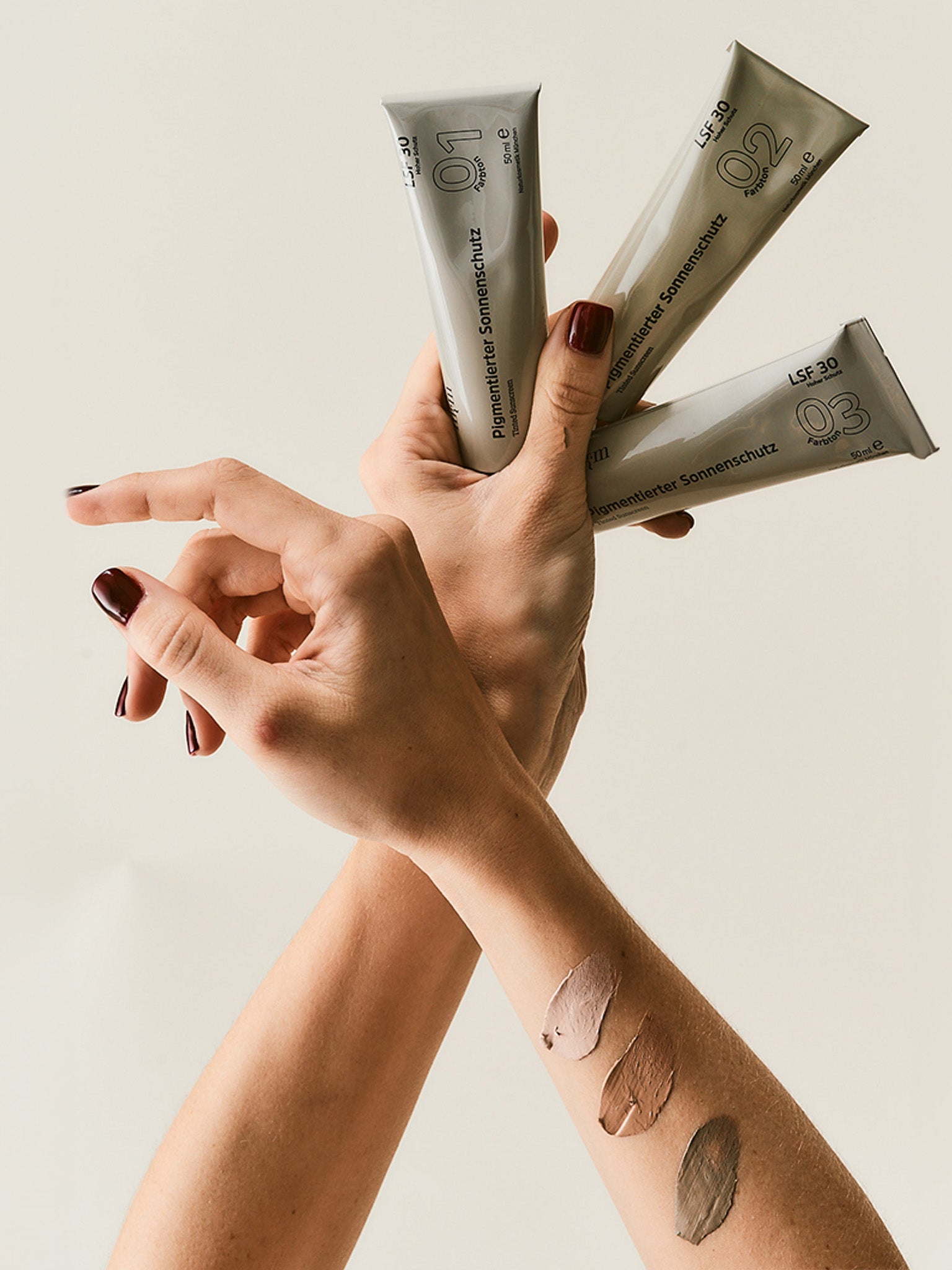 Hand hält alle drei Pigmentierten Sonnenschutze in einer Hand, auf der anderen Hand sind die Sonnenschutze aufgetragen