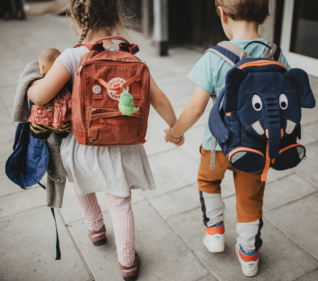 zwei Kinder mit Rucksäcken laufen Hand in Hand