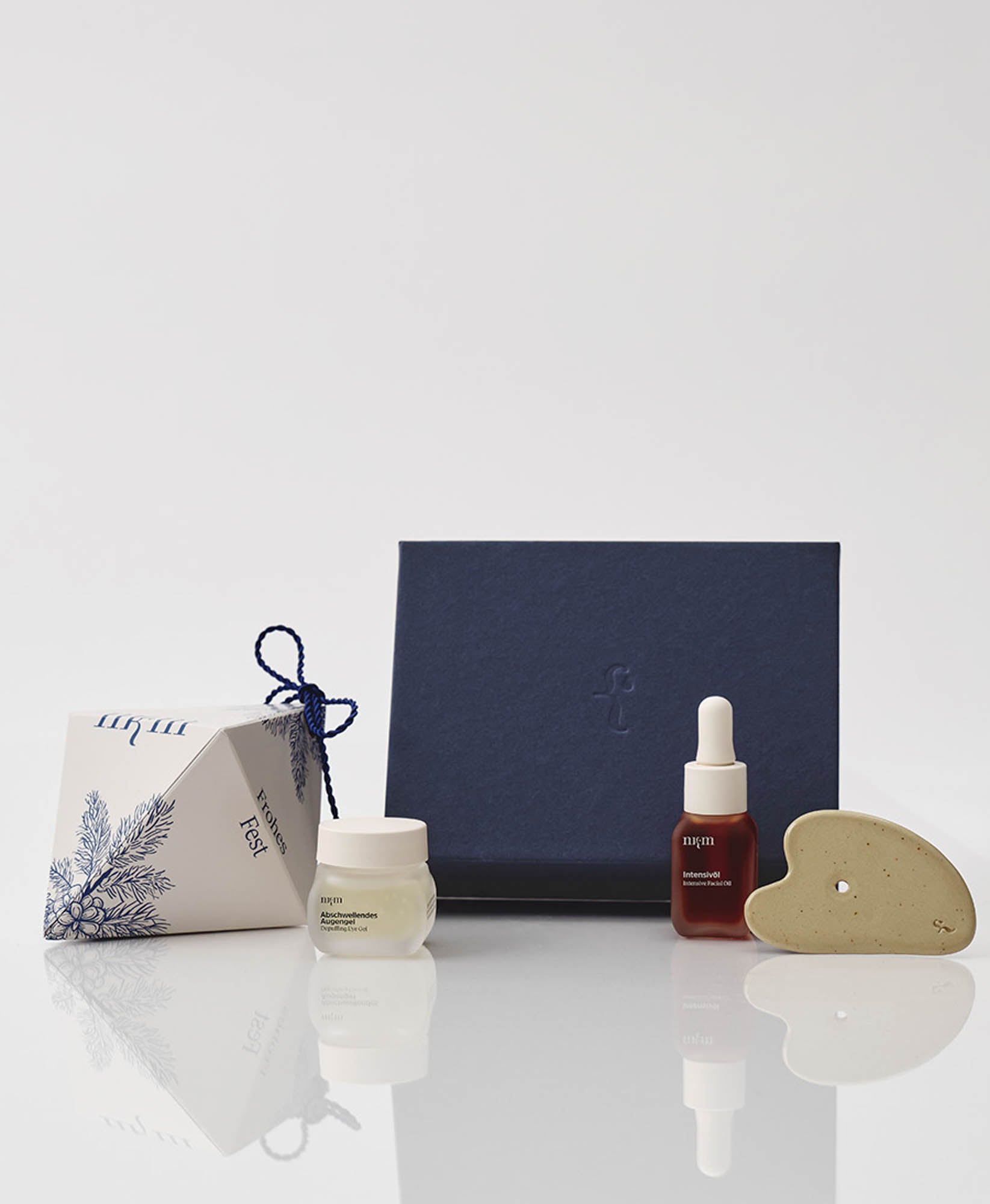 Blaue Geschenkbox und weihnachtliches Ornament, im Vordergrund das Abschwellende Augengel, Intensivöl und der Gua Sha von nkm