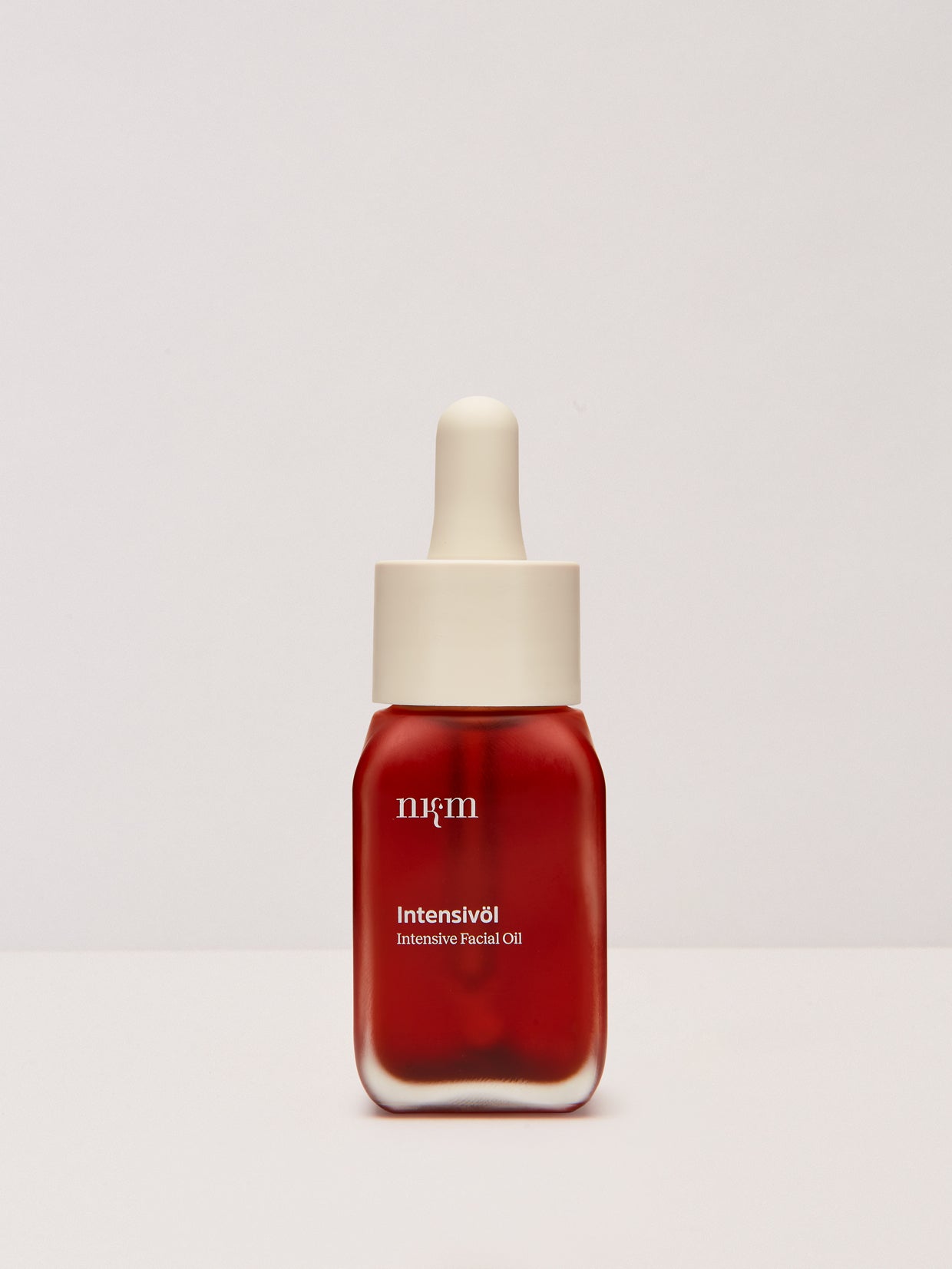 Eine rote Glastropfflasche von Intensivöl der nkm Naturkosmetik München GmbH mit pflegenden Ölen aus Hagebutte und Sanddorn auf hellem Grund.