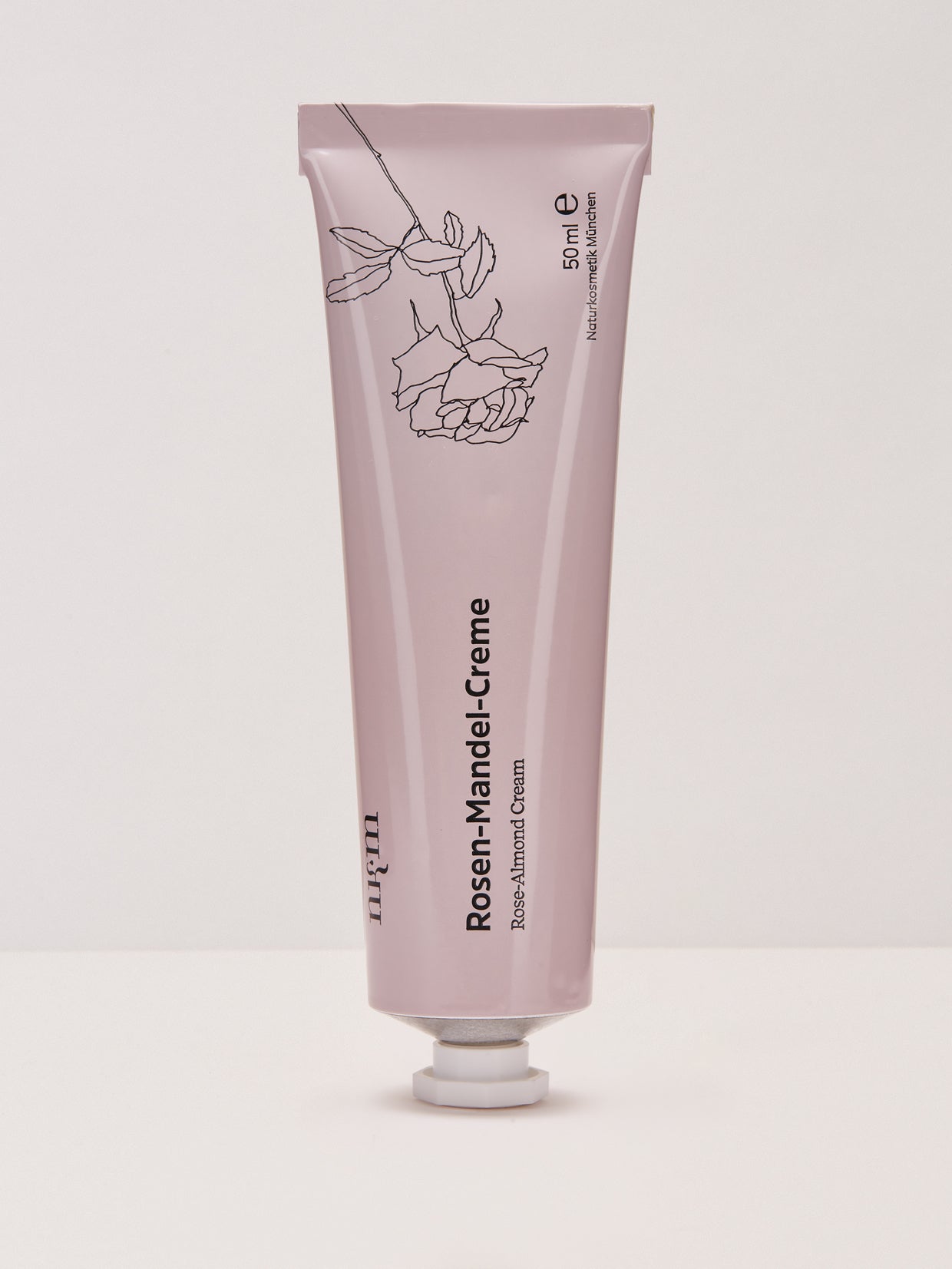 Die nkm Naturkosmetik München GmbH Rosen-Mandel-Creme in der rosa Tube mit Rosenmotiv und feuchtigkeitsförderndem Apfelwasser steht aufrecht auf einer weißen Fläche.
