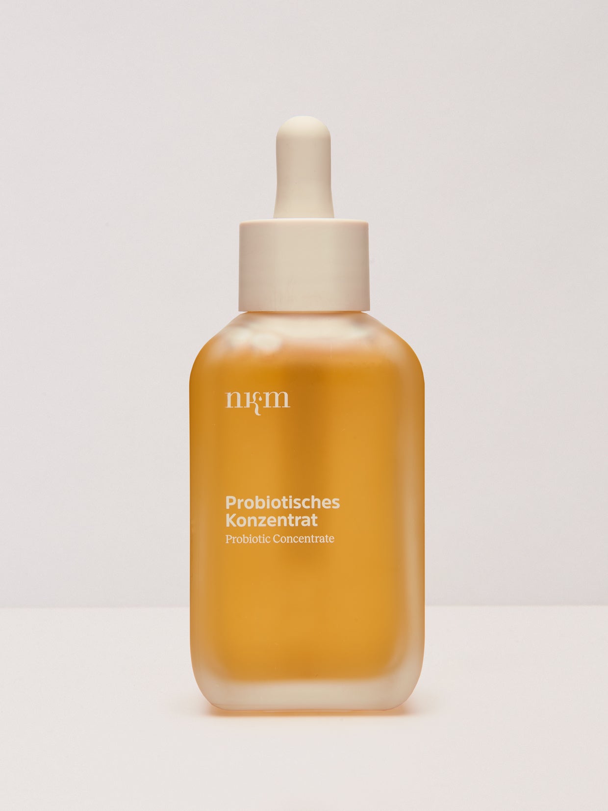Mattierte Tropfflasche mit bernsteinfarbener Flüssigkeit mit der Aufschrift Probiotisches Konzentrat von nkm Naturkosmetik München GmbH, mit probiotischem Milchsäureferment für die Hautbarriere, auf weißem Hintergrund.