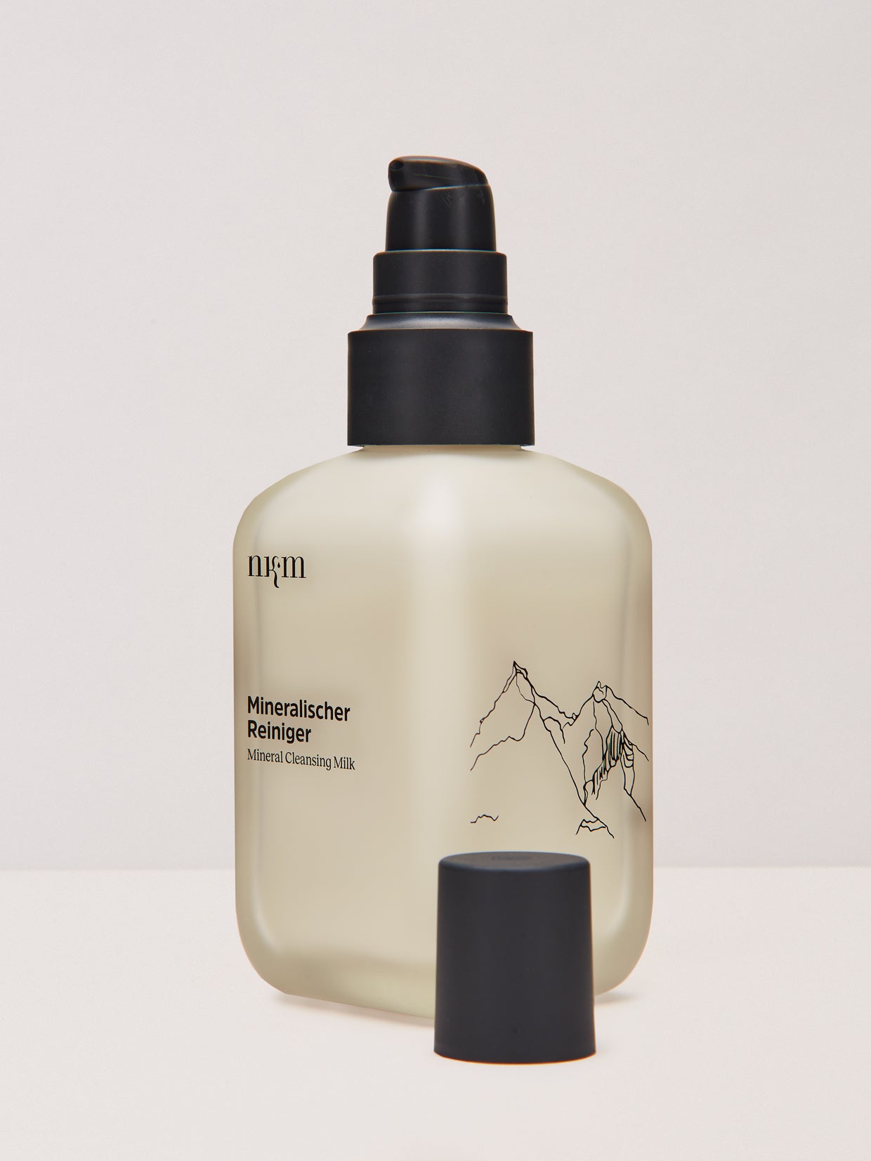 Eine Flasche Mineralischer Reiniger von nkm Naturkosmetik München GmbH mit schwarzer Pumpe und Kappe, Berg-Etiketten-Design. Ideal für sensible Haut, angereichert mit entzündungshemmendem Zink und Rügener Heilkreide.