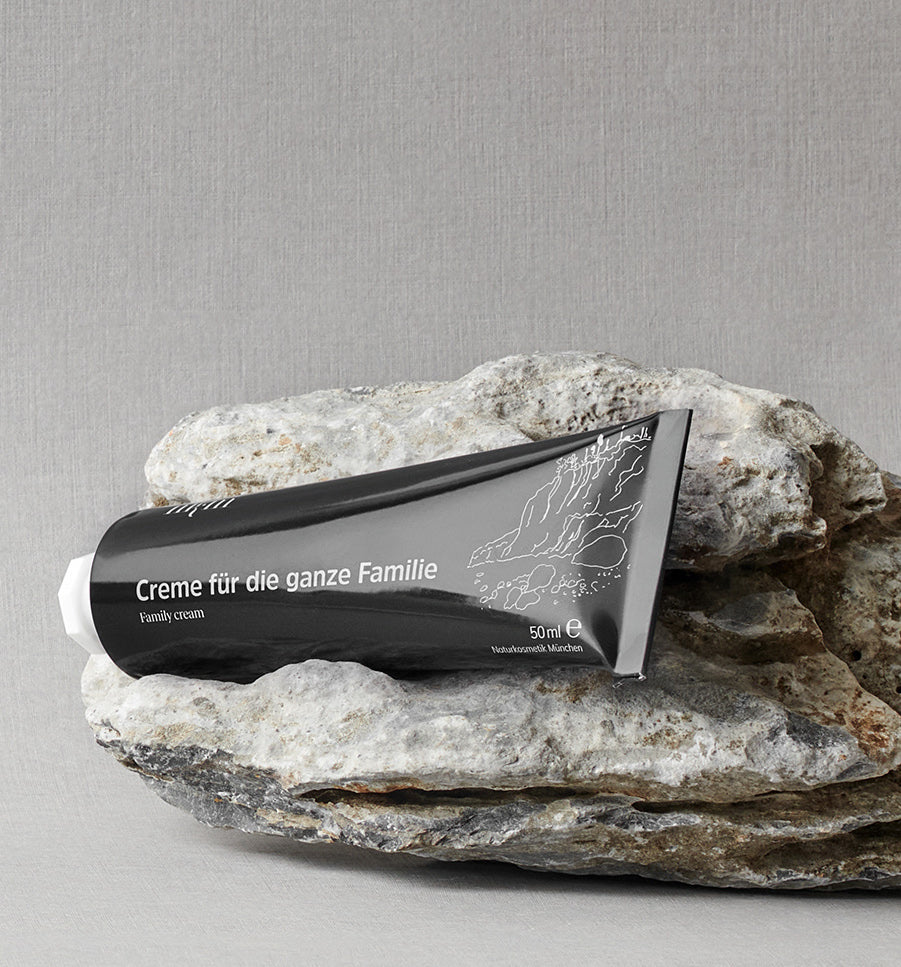Eine schwarze Tube mit der Aufschrift "Creme für die ganze Familie" der nkm Naturkosmetik München GmbH, bekannt für intensive Pflege, ruht auf zwei gestapelten grauen Steinen.