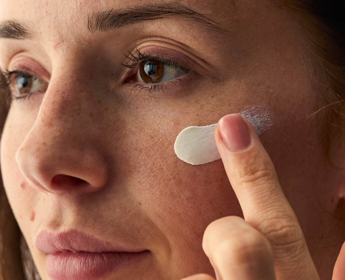 Close up von Anwendung einer weißen Creme im Gesicht.