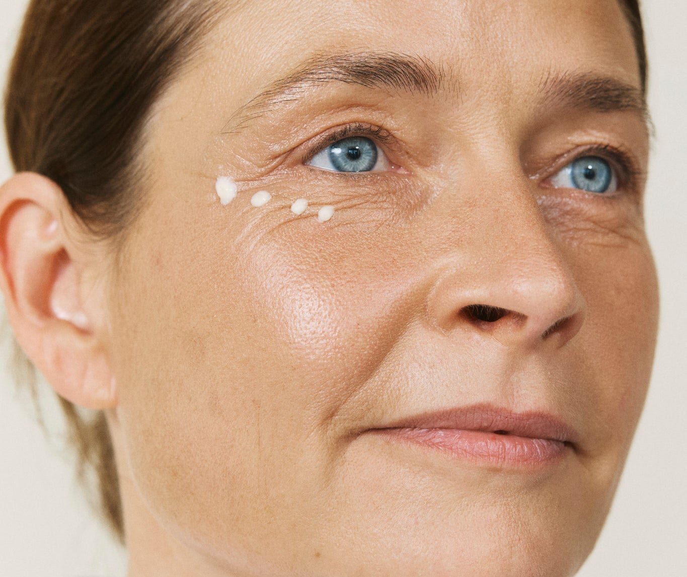 Eine Frau mit hellen blauen Augen, die eine Augencreme unter ihren Augen trägt