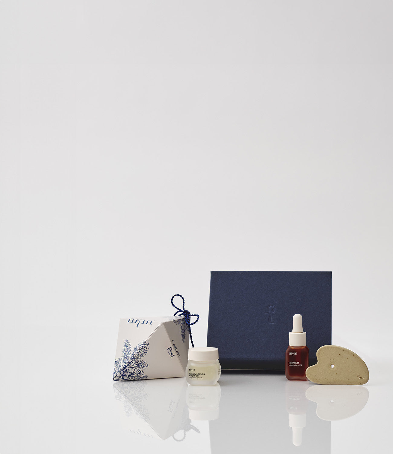 Weihnachtliches Ornament, blaue Geschenkbox und davor das Abschwellende Augengel, sowie das Intensivöl und der Gua Sha von nkm