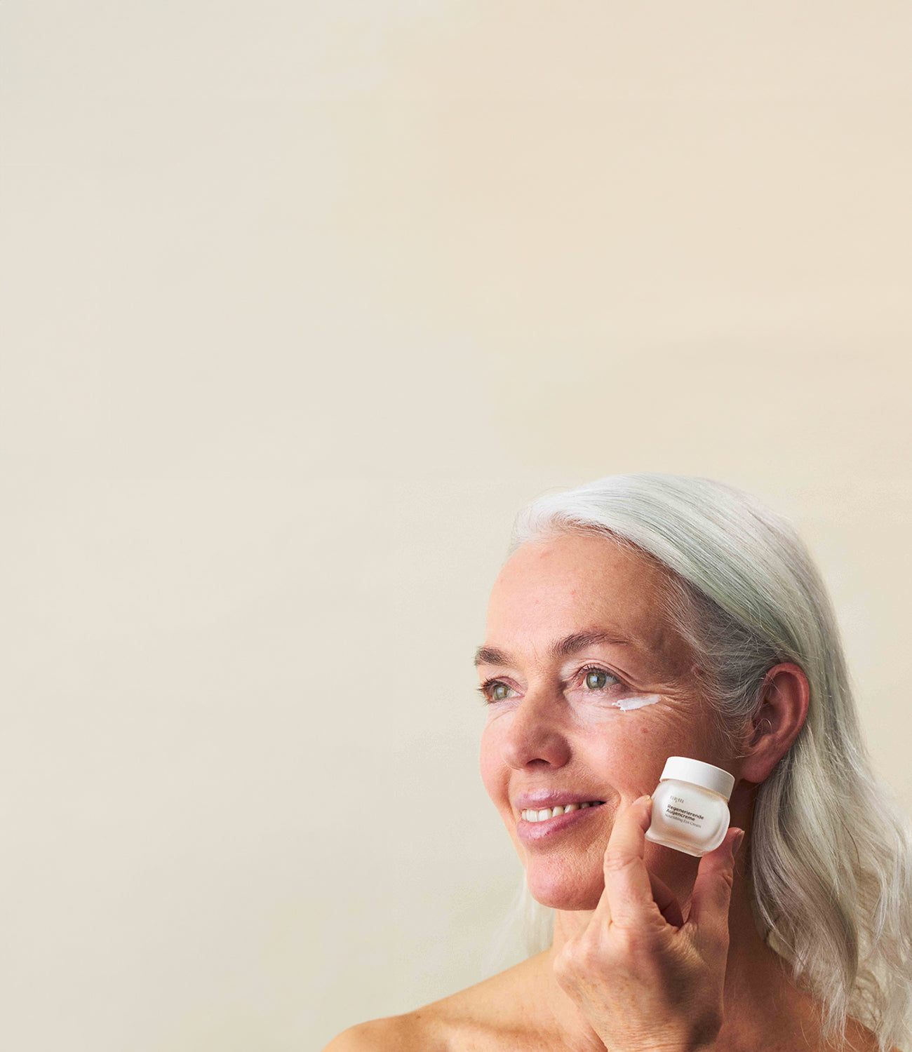 Eine Frau mit reifer Haut hält die Regenerierende Augencreme von nkm