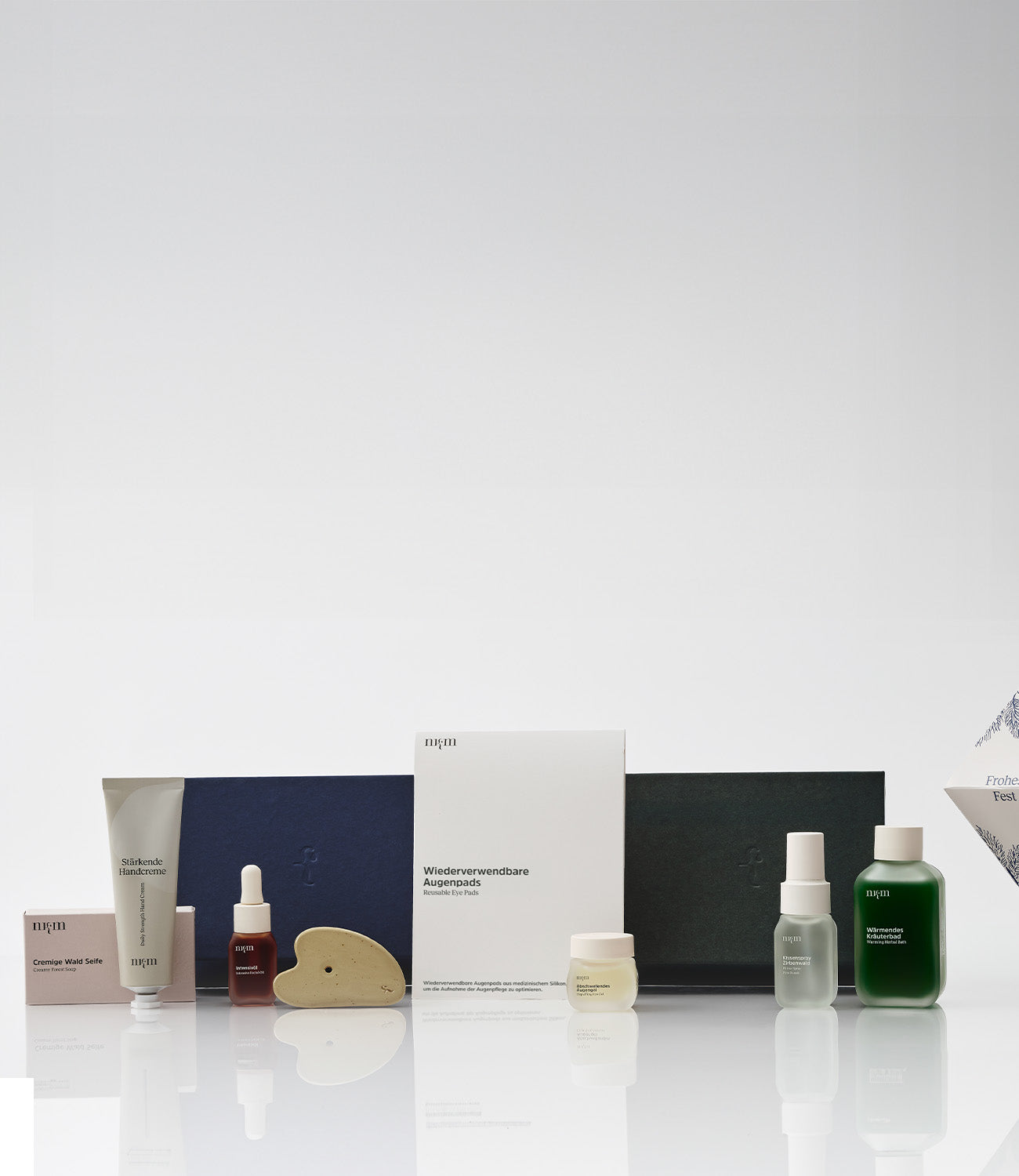 Blaue und grüne Weihnachtsbox, davor Cremige Wald Seife, Stärkende Handcreme, Intensivöl, Gua Sha, Wiederverwendbare Augenpads, Abschwellendes Augengel, Kissenspray Zirbenwald und Wärmendes Kräuterbad. Rechts das weihnachtliche Ornament.