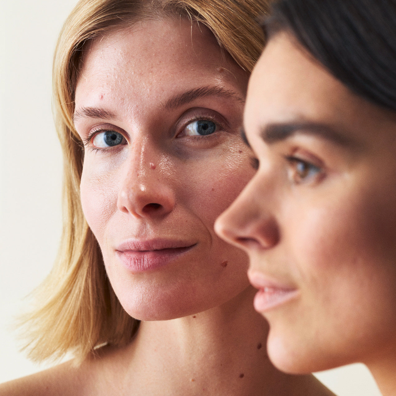 Zwei Frauen, die hintereinander stehen, die eine schaut nach links und die andere direkt in die Kamera